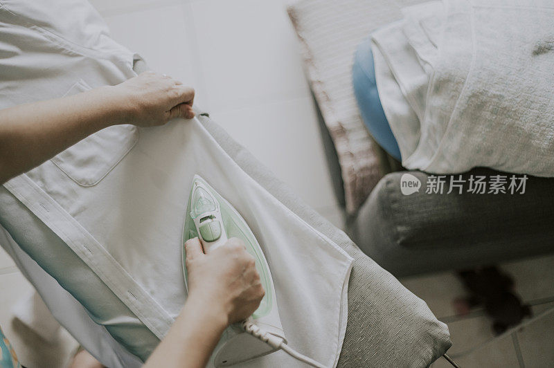 an asian chinese mid adult ironing his button down white shirt high angle view